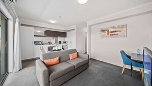 En moderne stue med en grå sofa, et spisebord med stole, et køkken i baggrunden og et stort abstrakt maleri på væggen.