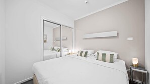 Et hotelværelse med en stor seng, et natbord med lampe, et spejl og en hylde på væggen.