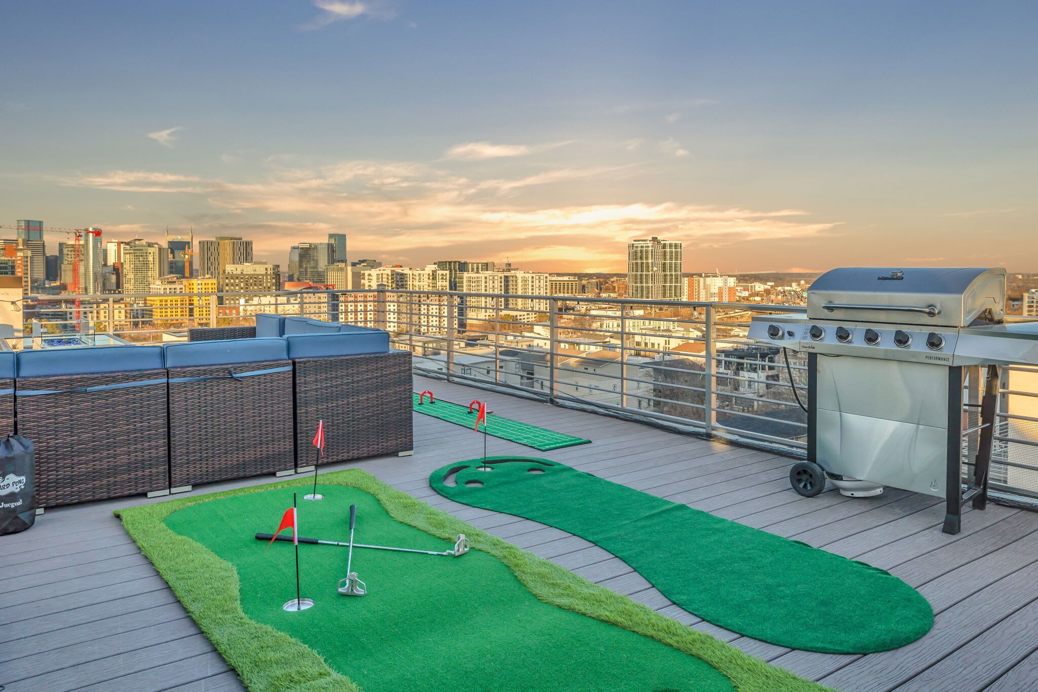 A rooftop with a miniature golf course, a barbecue grill, and a city skyline view.