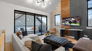 Un salon moderne avec un canapé, un pouf et un téléviseur à écran plat fixé au mur.