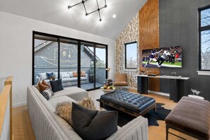 Ein modernes Wohnzimmer mit einer Couch, einem Hocker und einem an der Wand befestigten Flachbildfernseher.