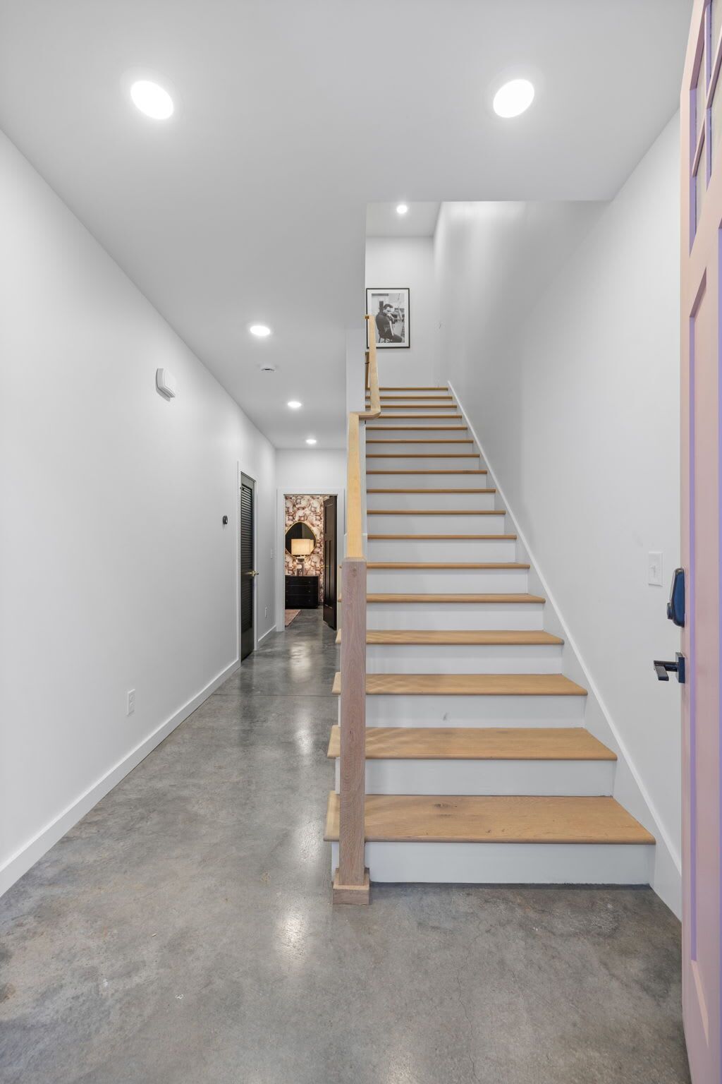 Un interior moderno con una escalera de madera, paredes blancas y suelo de hormigón.