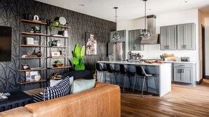 Eine moderne Küche mit einer zentralen Kochinsel, Barhocker und einer Sitzecke inklusive Sofa und Sesseln.