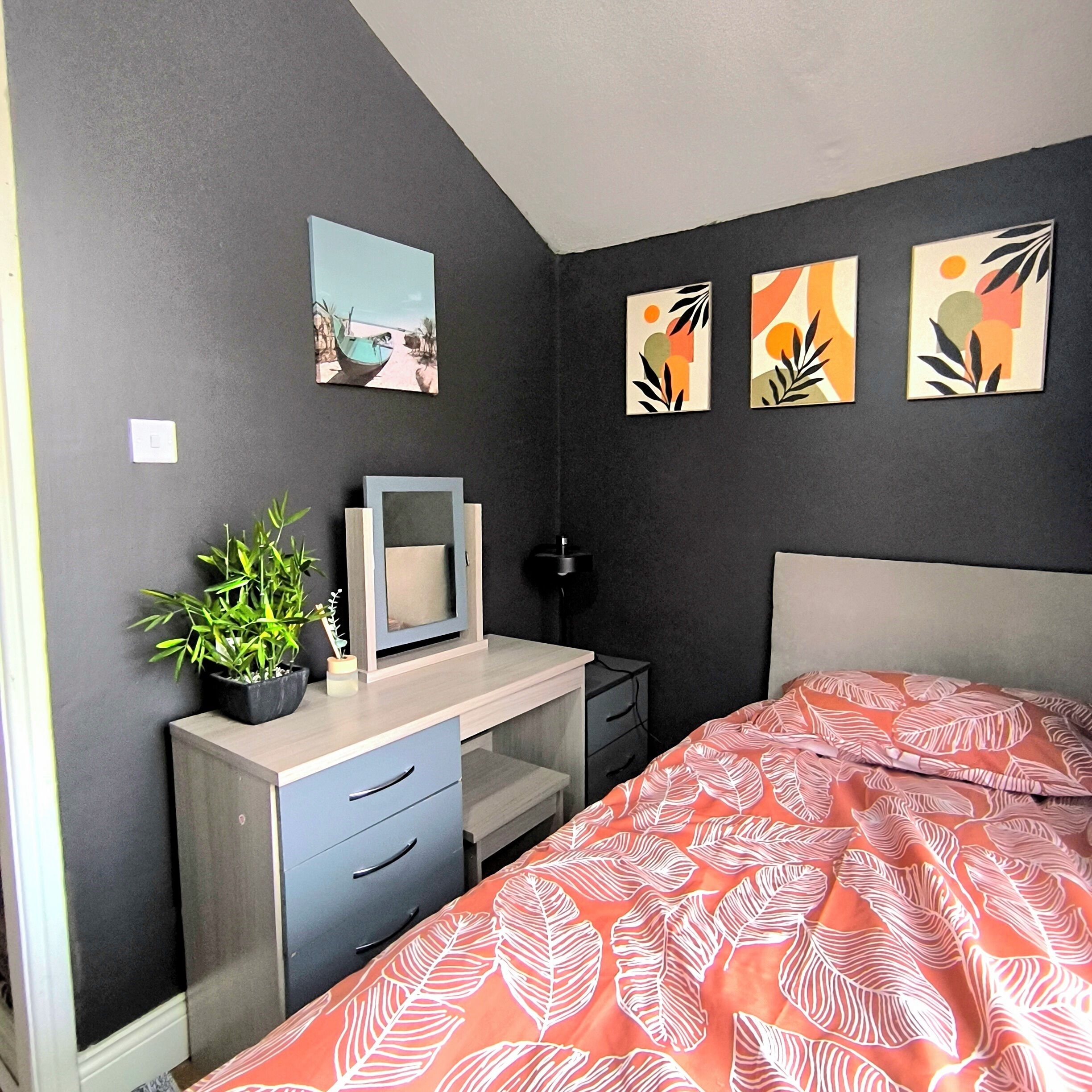 A bedroom with a bed, a desk, a chair, and a potted plant.