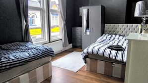 A bedroom with two beds, a wardrobe, a desk, and a window with curtains.
