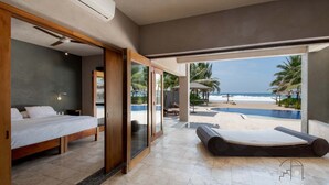 A bedroom with a bed, a large window, and a view of a pool and beach.