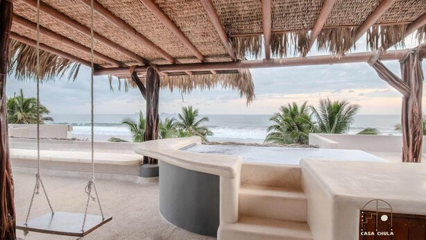 A beachside lounge with a thatched roof, a swing, and a view of the ocean.