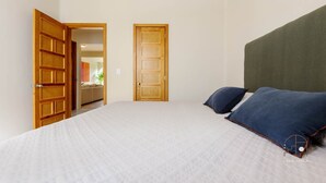 Een slaapkamer met een groot bed, twee kussens, een houten deur en uitzicht op een andere kamer.