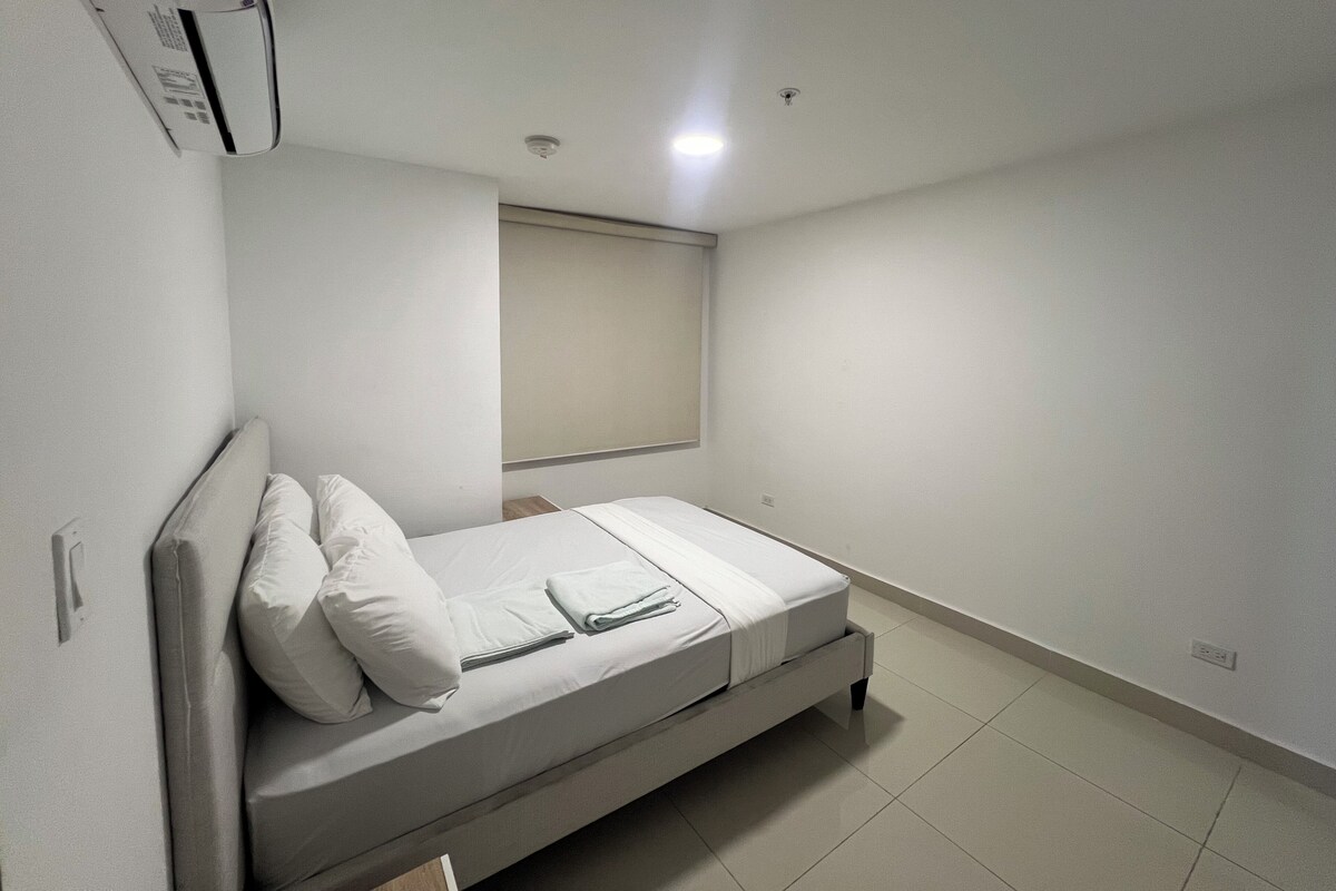 A single-bed room with a headboard, a window with blinds, a wall-mounted air conditioner, and a tiled floor.