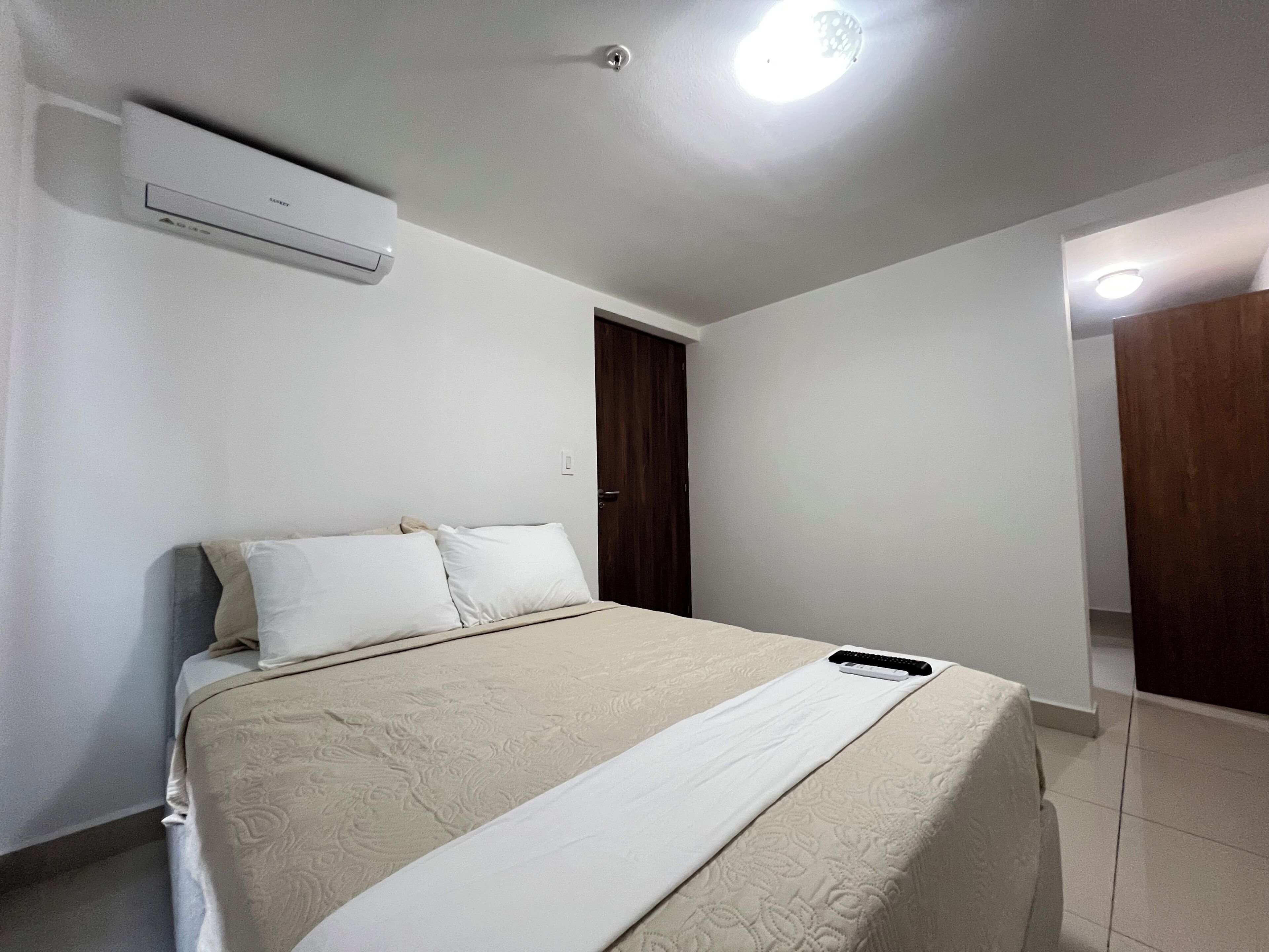 A bedroom with a bed, a ceiling light, and a wall-mounted air conditioner.