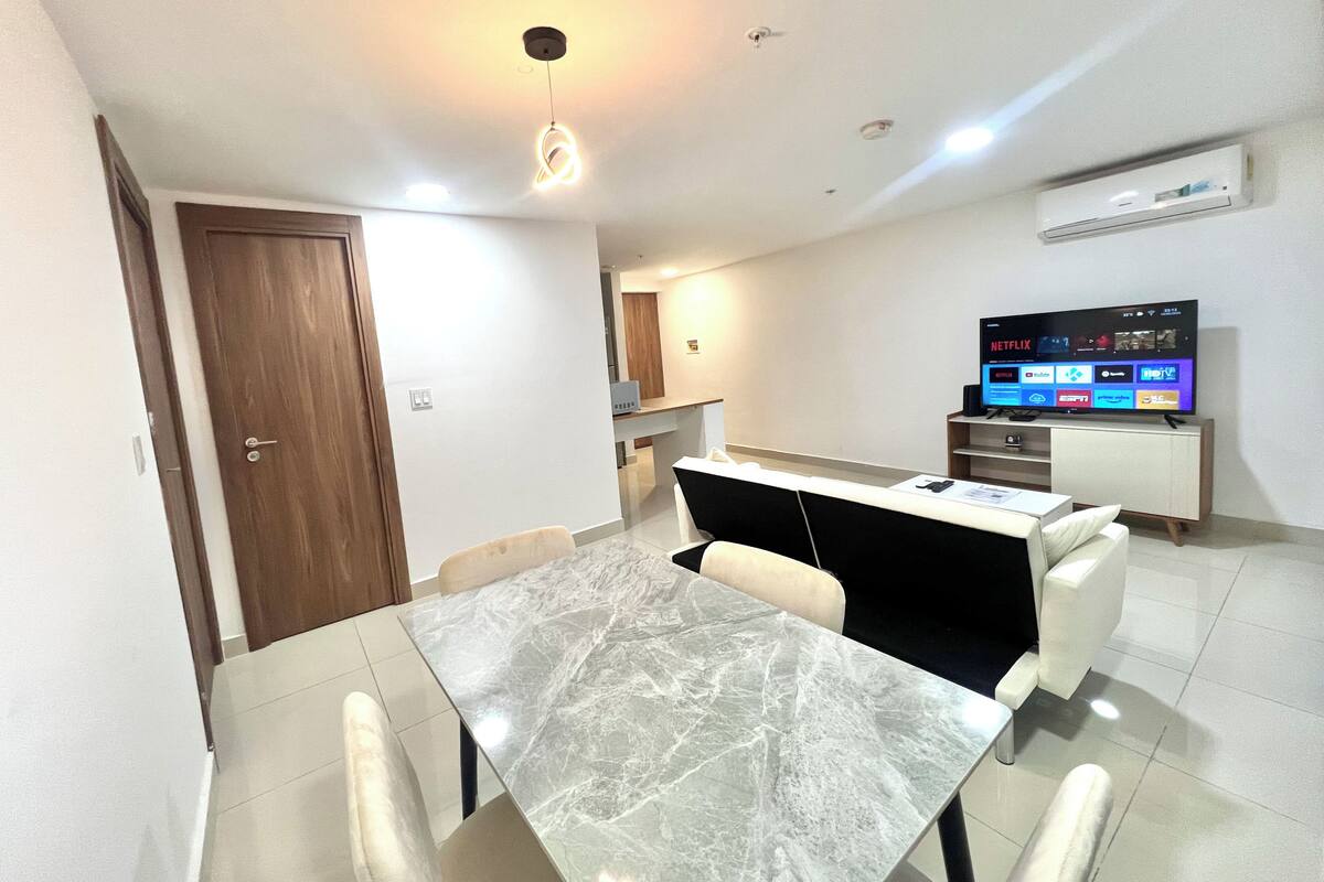 A modern living room with a marble dining table, a flat-screen TV, and a built-in air conditioning unit.