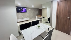 Un espace repas moderne avec une table en marbre, des chaises grises, une console blanche et un téléviseur fixé au mur.