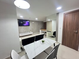 A modern dining area with a marble table, grey chairs, a white console, and a TV mounted on the wall.