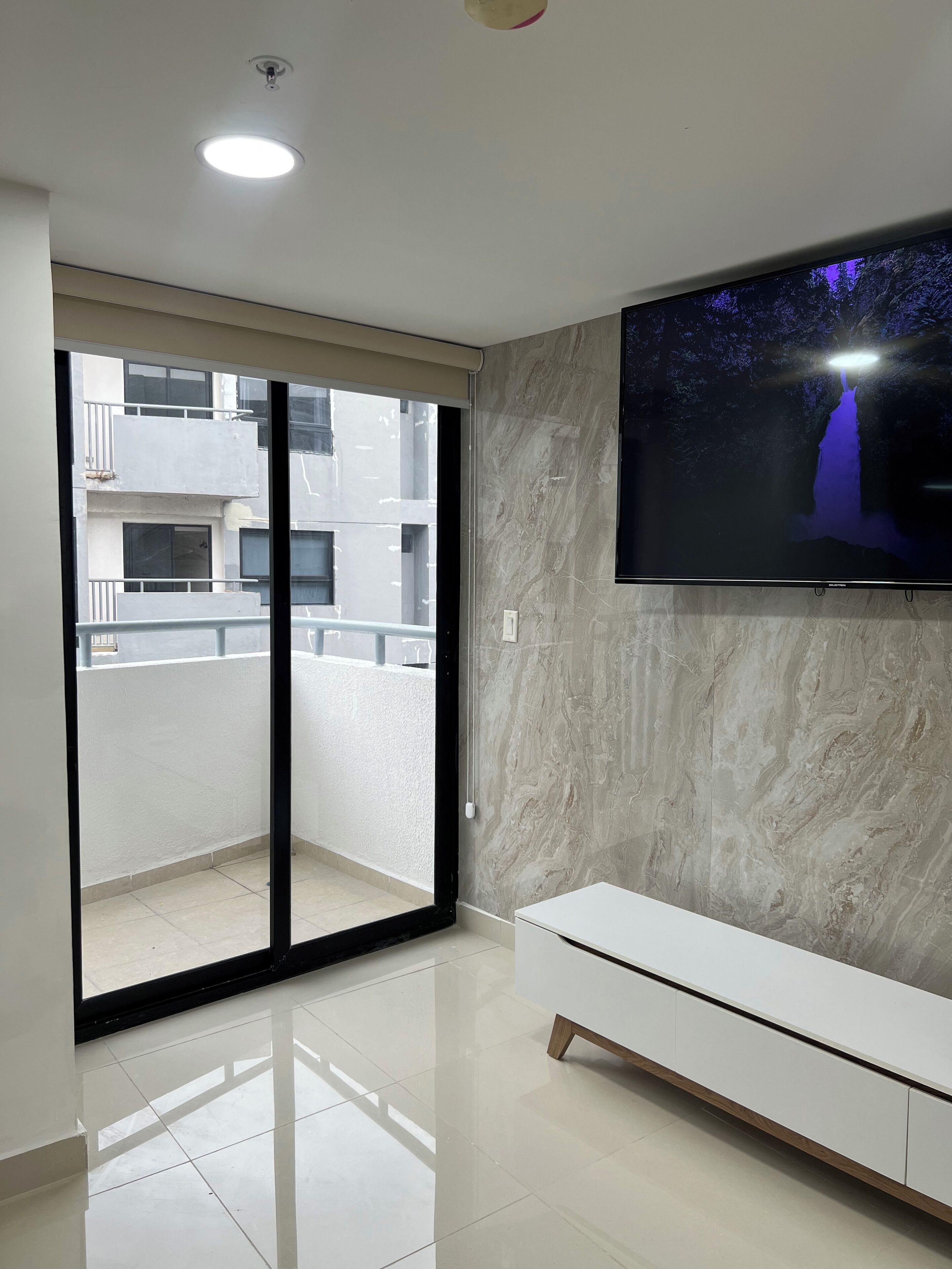 A modern living room with a large TV mounted on the wall, a sliding glass door leading to a balcony, and a white console table.