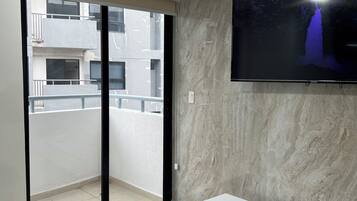 A modern living room with a large TV mounted on the wall, a sliding glass door leading to a balcony, and a white console table.