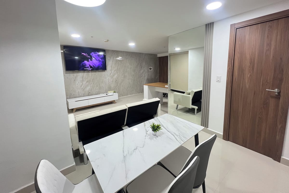 A modern dining area with a marble table, white chairs, a white console, and a TV mounted on the wall.
