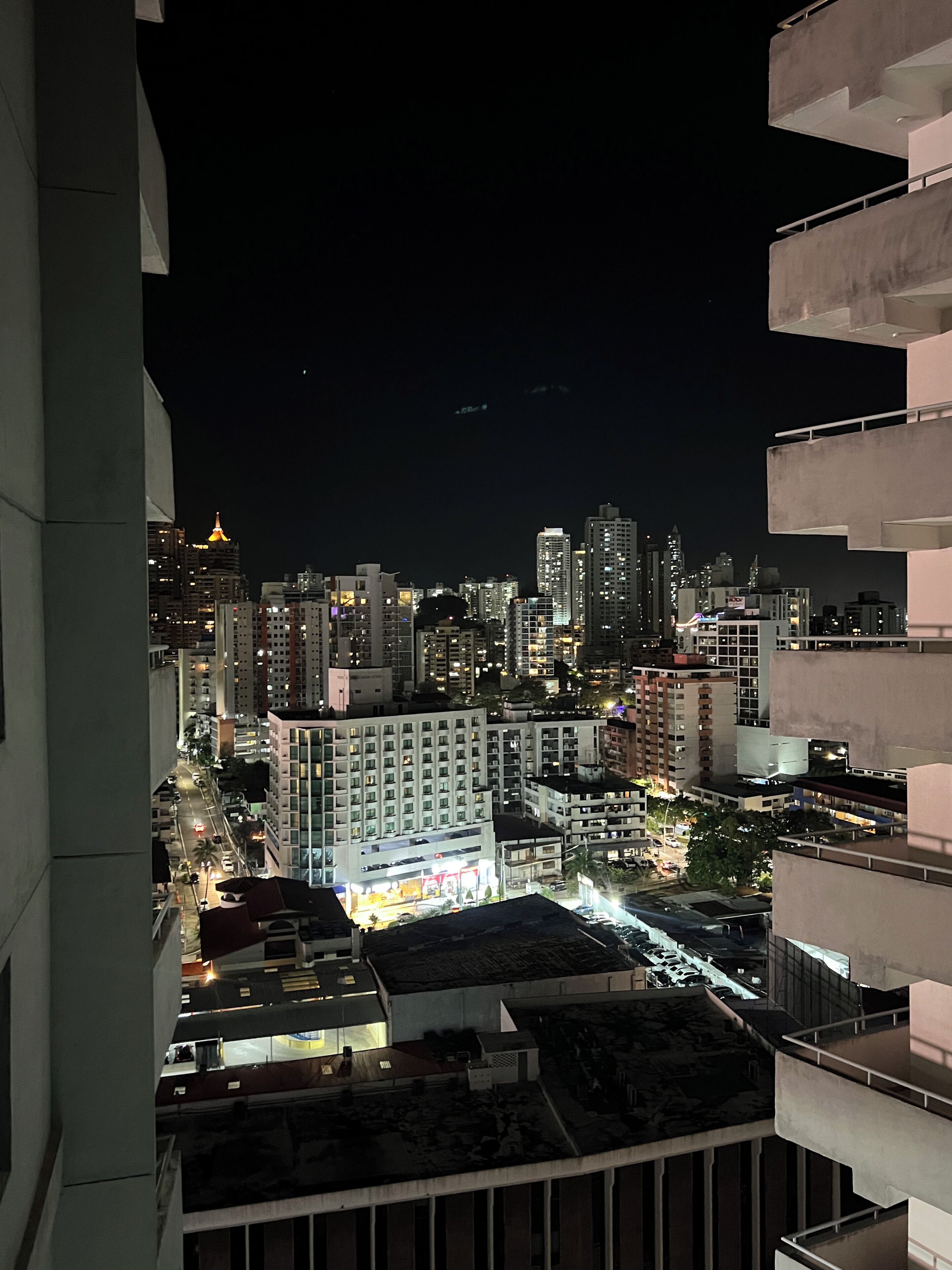 Un paisaje urbano nocturno con rascacielos, una torre destacada iluminada y una calle concurrida abajo.