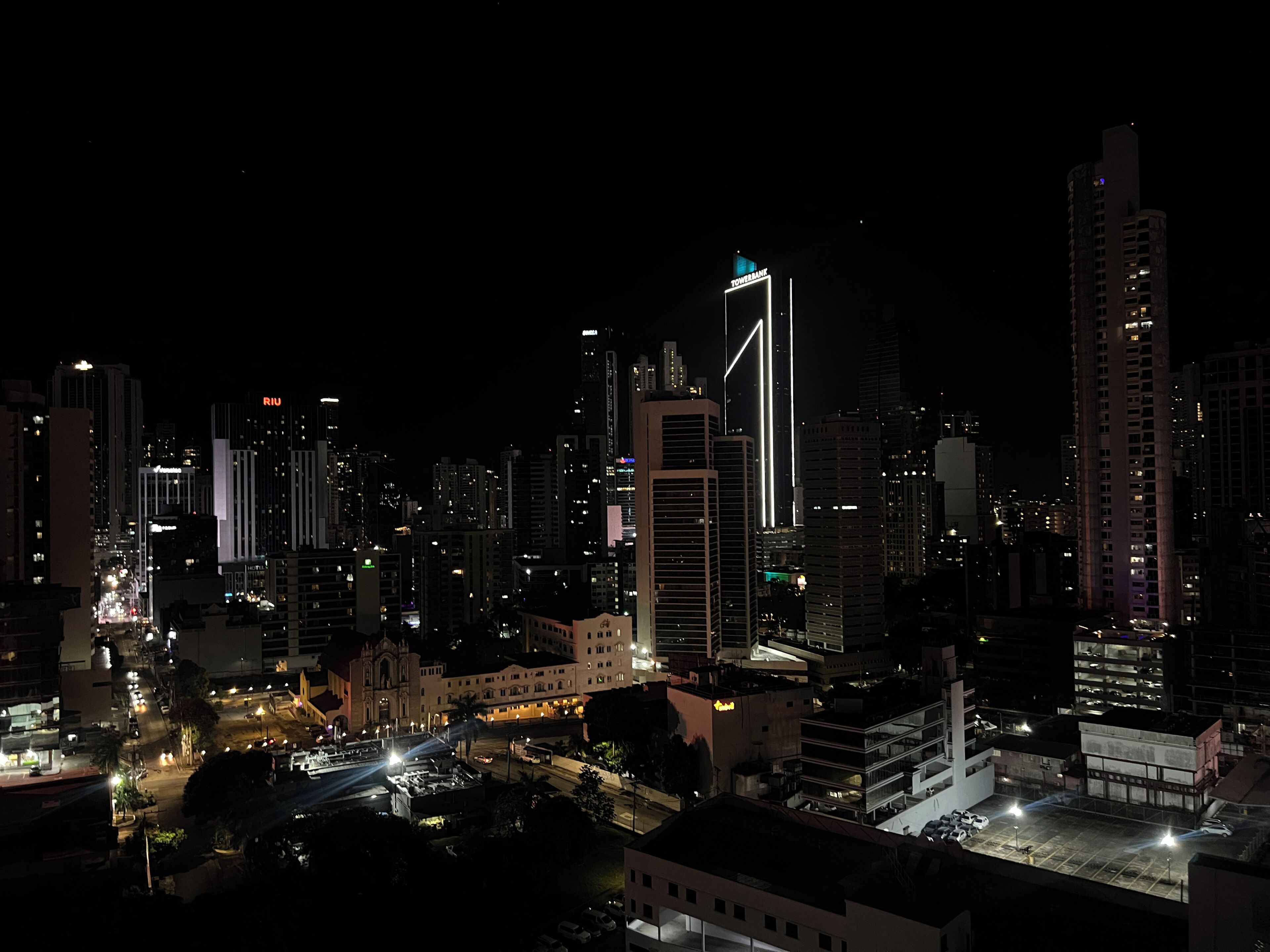 A nighttime cityscape with illuminated buildings, a prominent tower, and a cathedral-like structure.