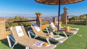 Eine Dachterrasse mit vier Liegestühlen, einem Tisch mit einer Zeitschrift, einem Korb und einer Weinflasche, mit Blick auf eine schöne Landschaft.