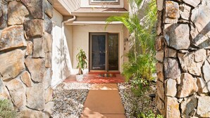 A house with a stone exterior, a front door, and a small garden area with plants and a pathway. - Tampa Oasis: Pool & Hot Tub Retreat for Families (Tampa)