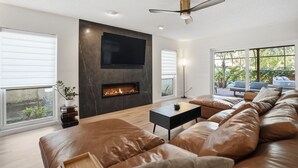A modern living room with a fireplace, leather sofa, and a large TV. - Tampa Oasis: Pool & Hot Tub Retreat for Families (Tampa)