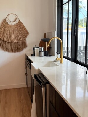 A modern kitchen with a white countertop, stainless steel appliances, and a gold faucet. - Peaceful Nelson Bay Retreat with Boutique Flair (Nelson Bay)