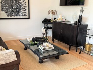 A living room with a glass coffee table, a black sofa, a black cabinet, and a framed artwork on the wall. - Peaceful Nelson Bay Retreat with Boutique Flair (Nelson Bay)