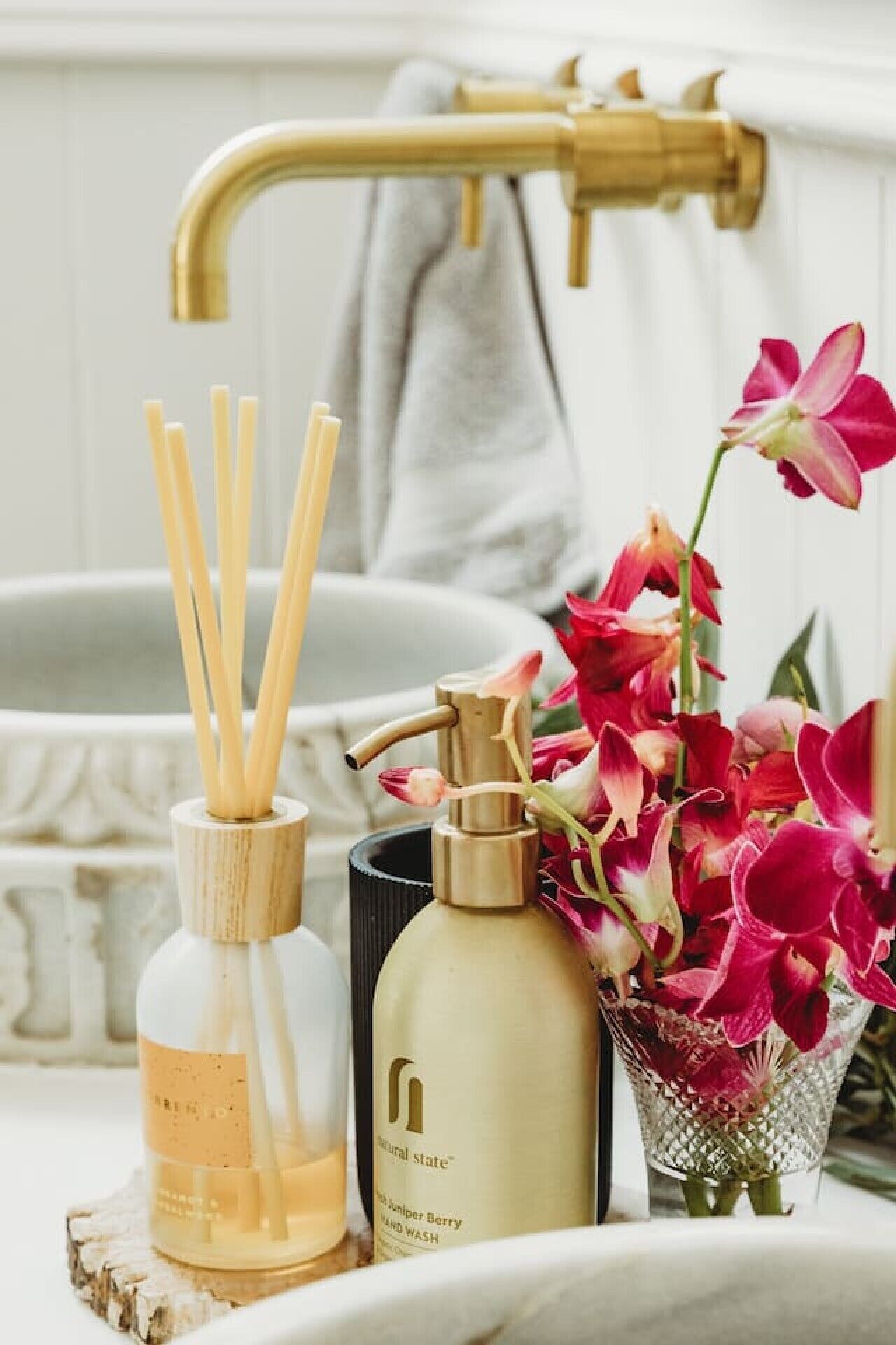 Un meuble-lavabo de salle de bain avec un robinet doré, un flacon de savon liquide pour les mains et un vase en verre contenant des fleurs.