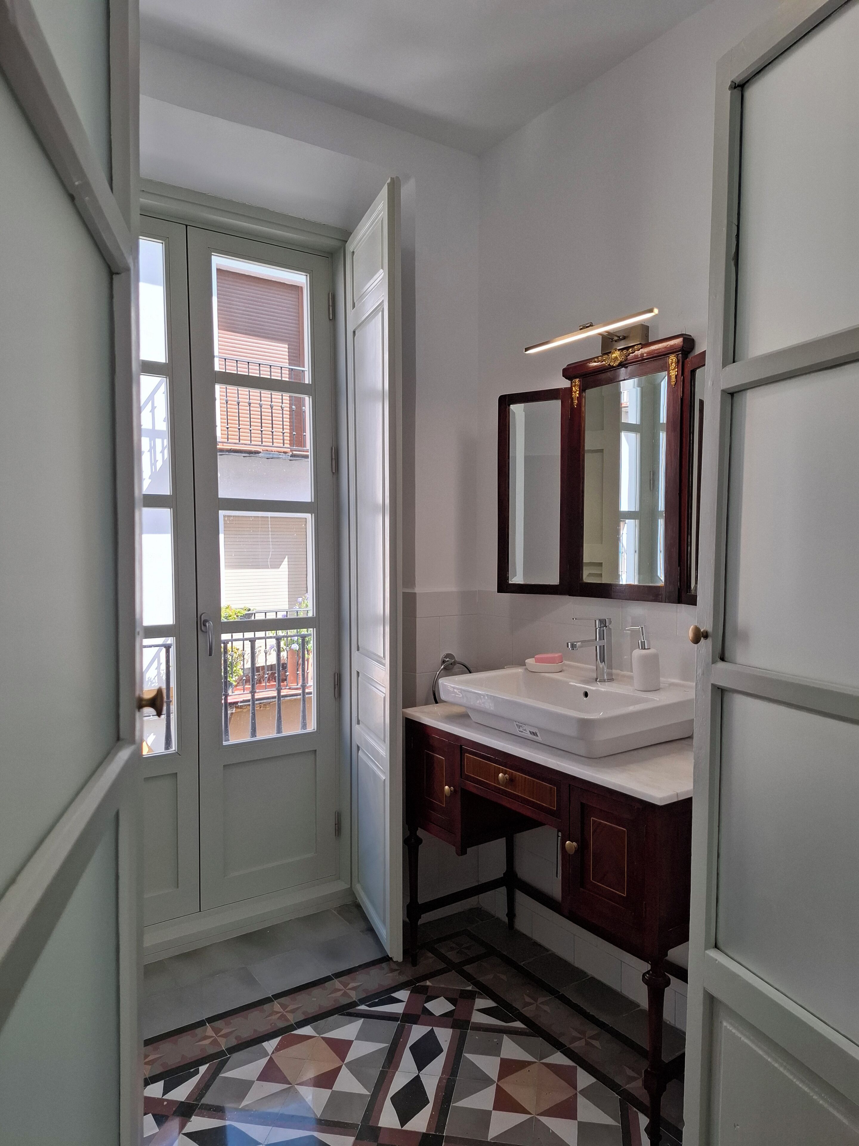 A bathroom with a white sink, a mirror, and a patterned floor.