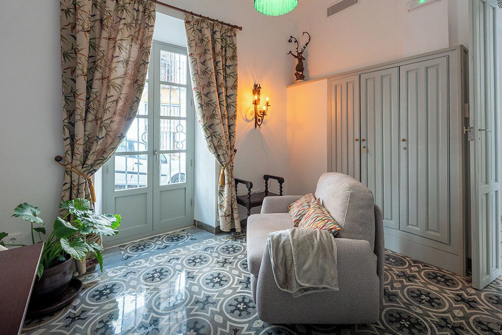 Una habitación con baldosas de suelo estampadas, un sofá con una manta, un aplique en la pared y una puerta con un armario azul claro.