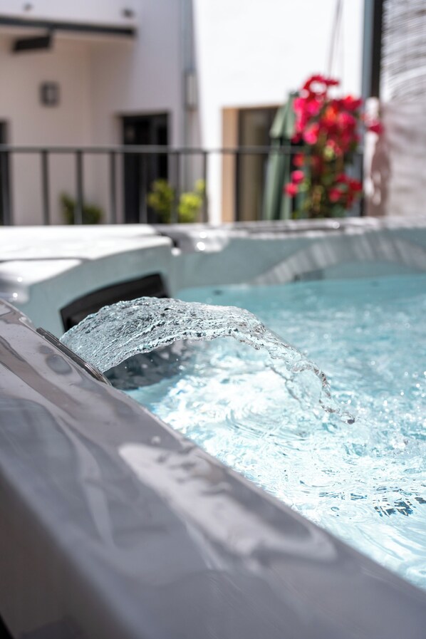A hot tub with water flowing out, a white building in the background, and a red flower in a pot.