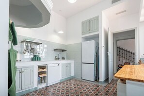 A kitchen with white cabinets, a refrigerator, a wooden countertop, and a patterned floor.