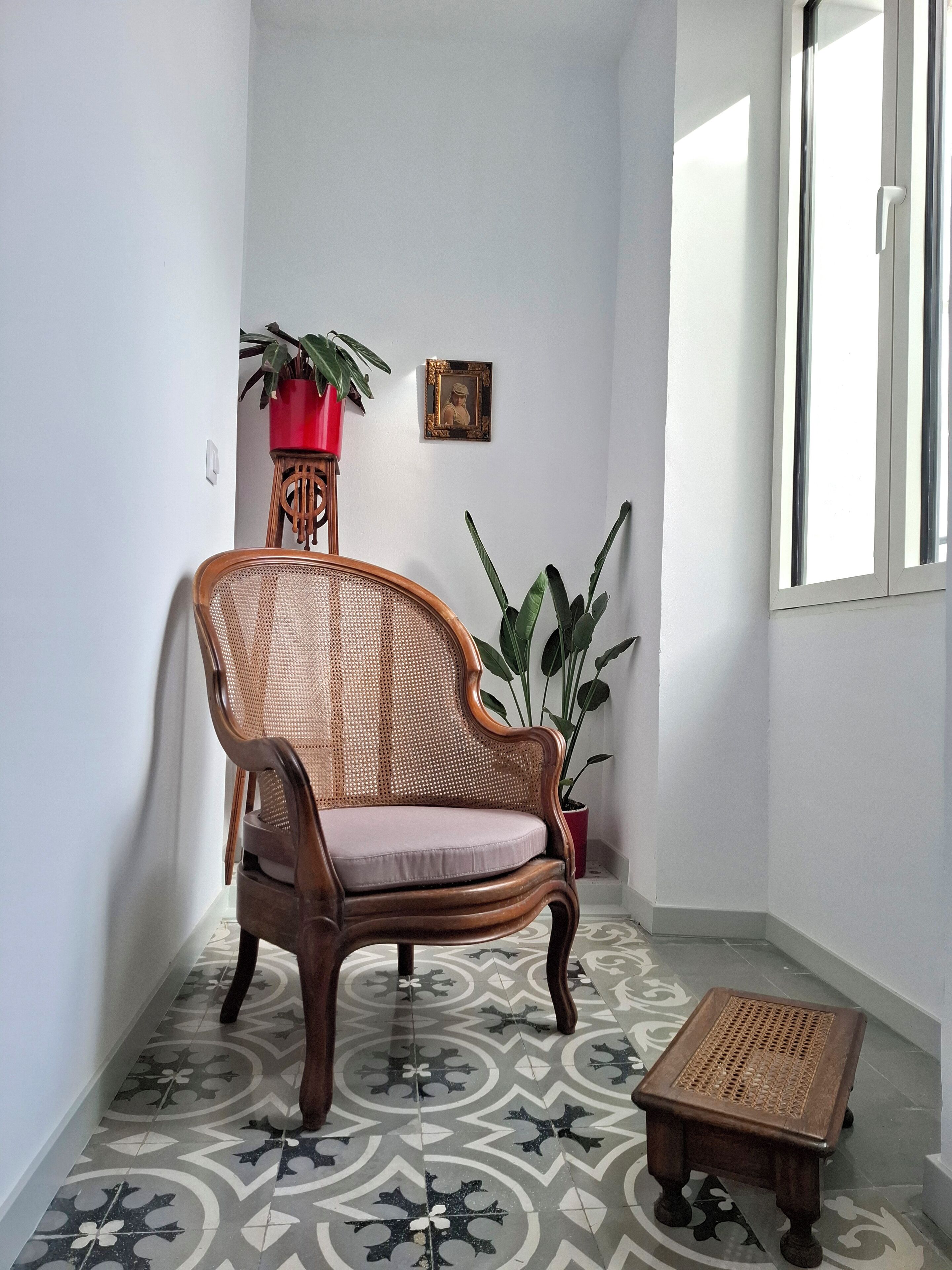 Una stanza d'angolo con una sedia in rattan, un tavolino e due piante in vaso.