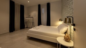 Um quarto moderno com uma cama bem arrumada, uma pequena mesa de cabeceira com abajur e luminária na parede.