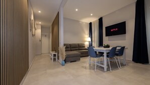 Uma sala de estar moderna com sofá, mesa de jantar, cadeiras, TV na parede e luminária.