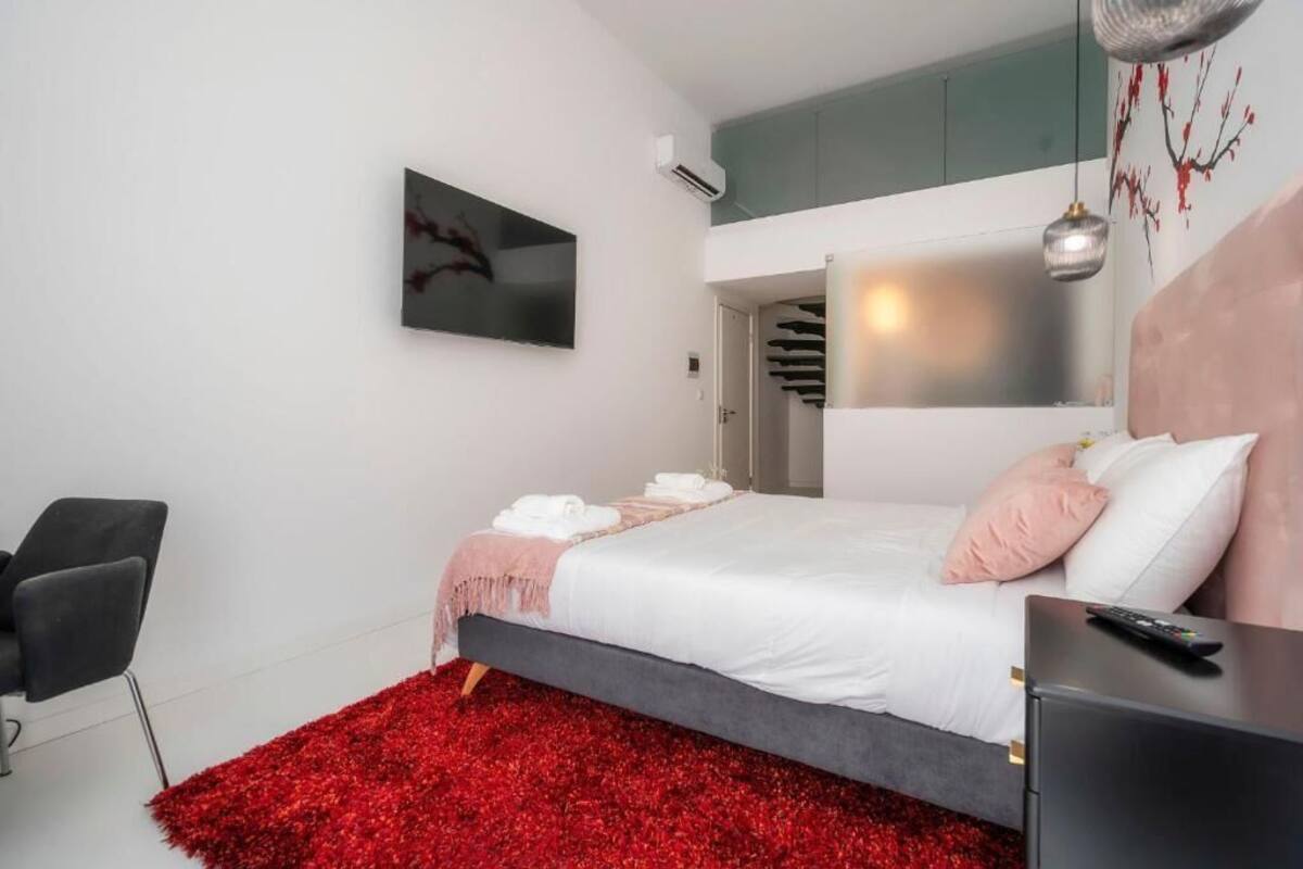 A modern bedroom with a bed, a red rug, a TV, and a painting on the wall.
