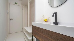 Ein modernes Badezimmer mit einem weißen Waschtisch, einem schwarzen Wasserhahn und einer kleinen Vase mit gelben Blumen.