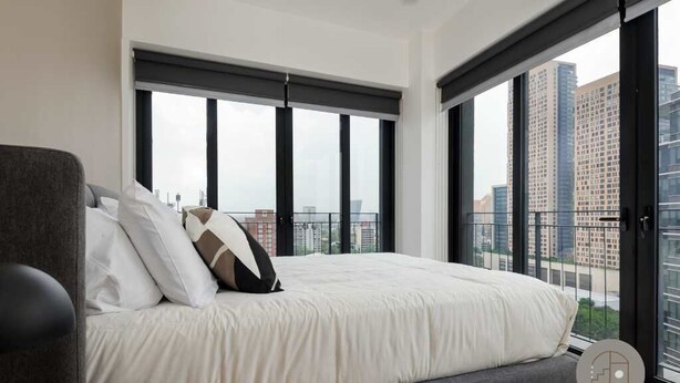 A modern bedroom with a large bed, a grey armchair, and a view of tall buildings through floor-to-ceiling windows. - Magnificent Apartment in the Heart Nuevo Polanco (Mexico City)