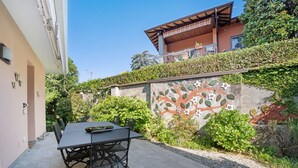 A patio with a table and chairs, a decorative wall with a tree mural, and a building with a balcony.