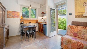 A modern kitchen with a dining table, chairs, a refrigerator, and a window overlooking greenery.
