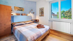 A bedroom with a bed, wooden wardrobe, wall art, and a window with a view.