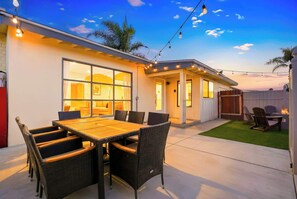 A patio with a wooden table and wicker chairs, a covered outdoor seating area, and a view of the house. - Stylish Retreat Near Mission Bay with Games & Firepit (San Diego)