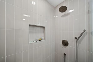 A modern shower area with a handheld showerhead, a wall-mounted faucet, and a shelf with toiletries. - Stylish Retreat Near Mission Bay with Games & Firepit (San Diego)