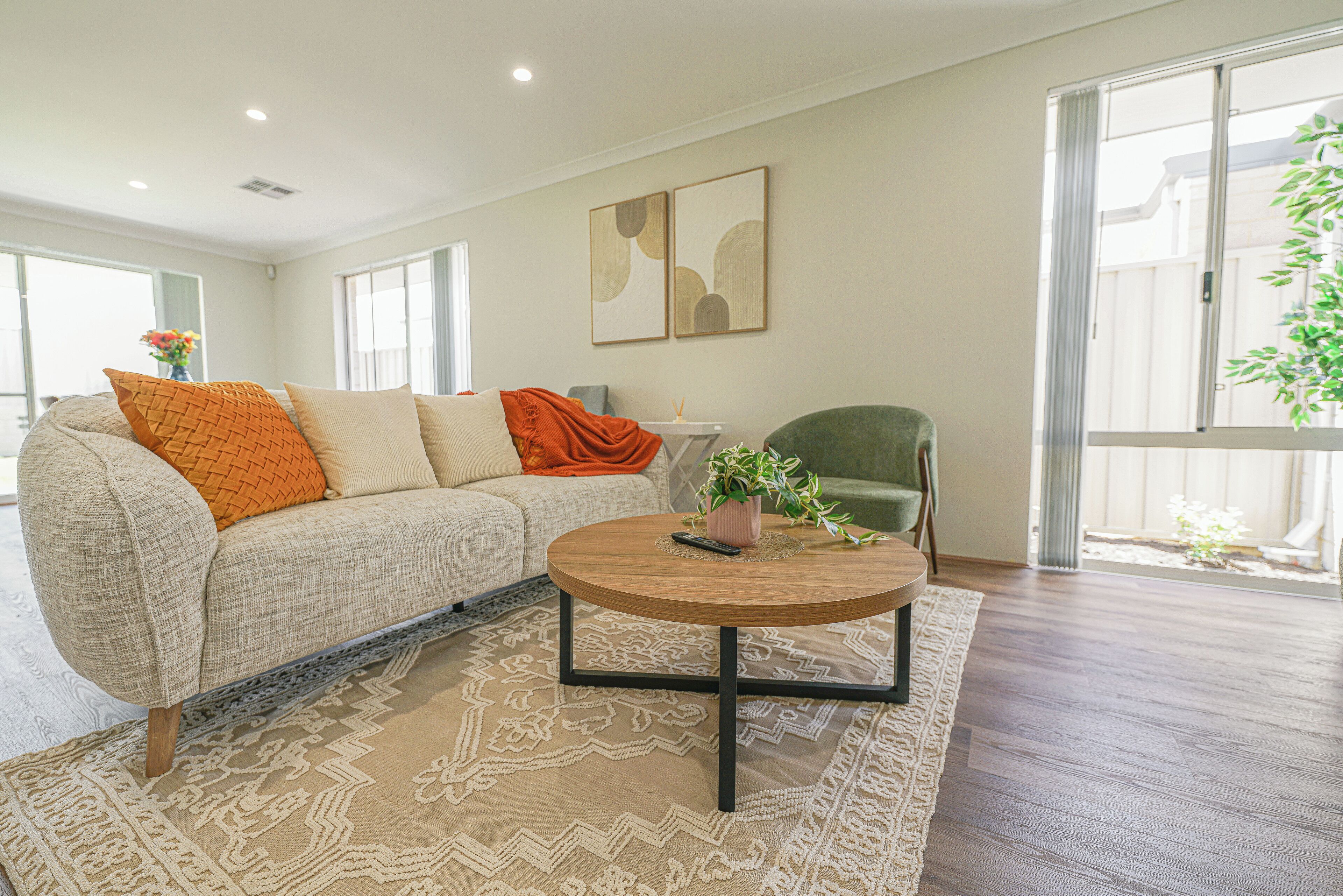A living room with a sofa, a round coffee table, and a chair. There is a large window and a plant on the windowsill.