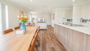 Een moderne keuken met een houten kookeiland, een eethoek met een houten tafel en stoelen, en een televisie op de achtergrond.