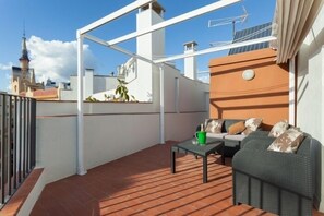 A rooftop terrace with a sofa and table, a green bucket, and a view of city buildings. - Rental unit in Sitges · ★4.92 · 1 bedroom · 1 bed · 1 bath (Sitges)