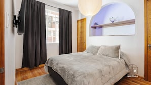 Ein Schlafzimmer mit einem Bett, einem großen Fenster mit Vorhängen, einer Holztür und einem an der Wand befestigten Regal mit Dekoration.