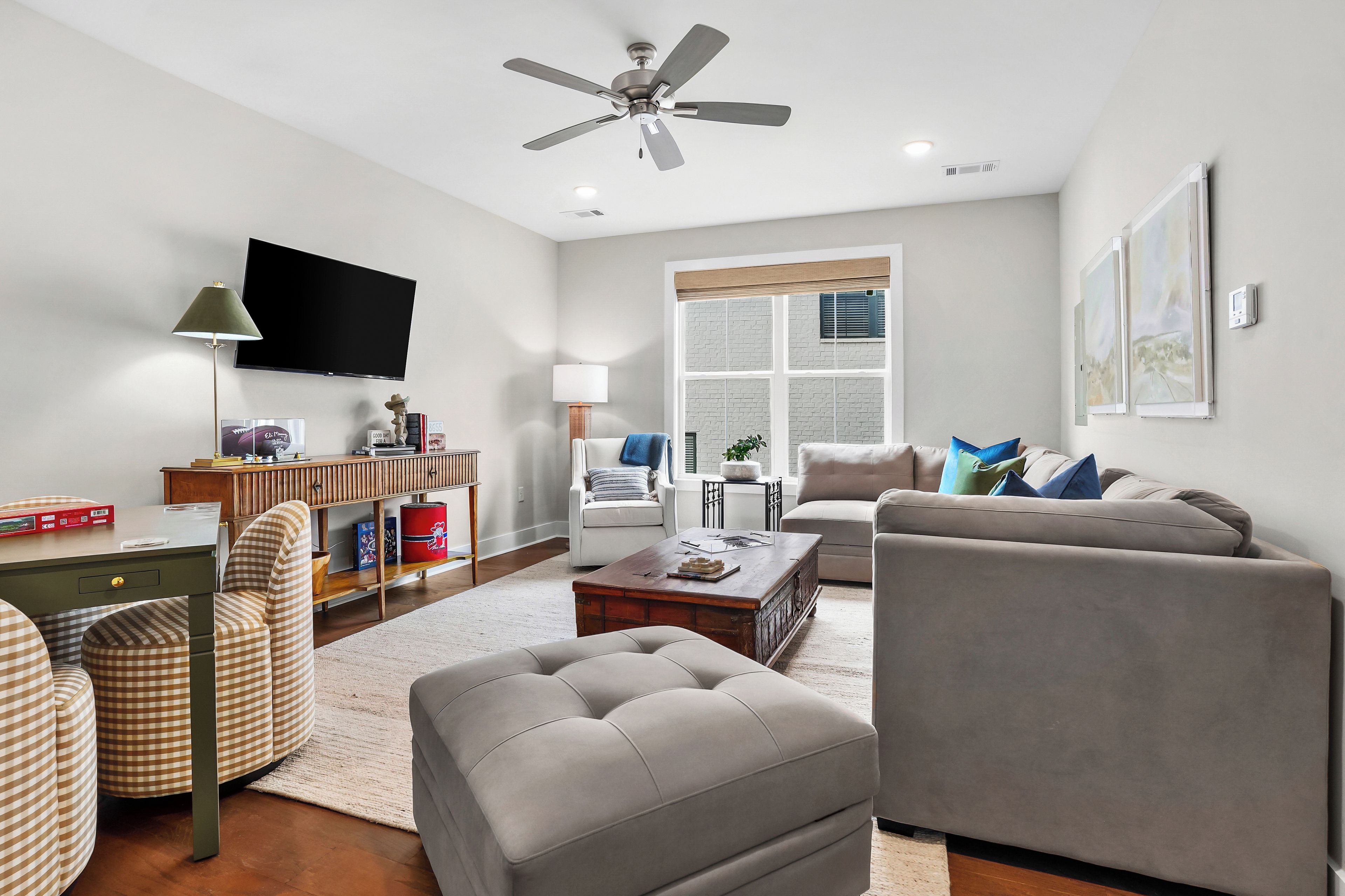 A modern living room with a flat-screen TV, a ceiling fan, a sofa, a coffee table, and a bookshelf.