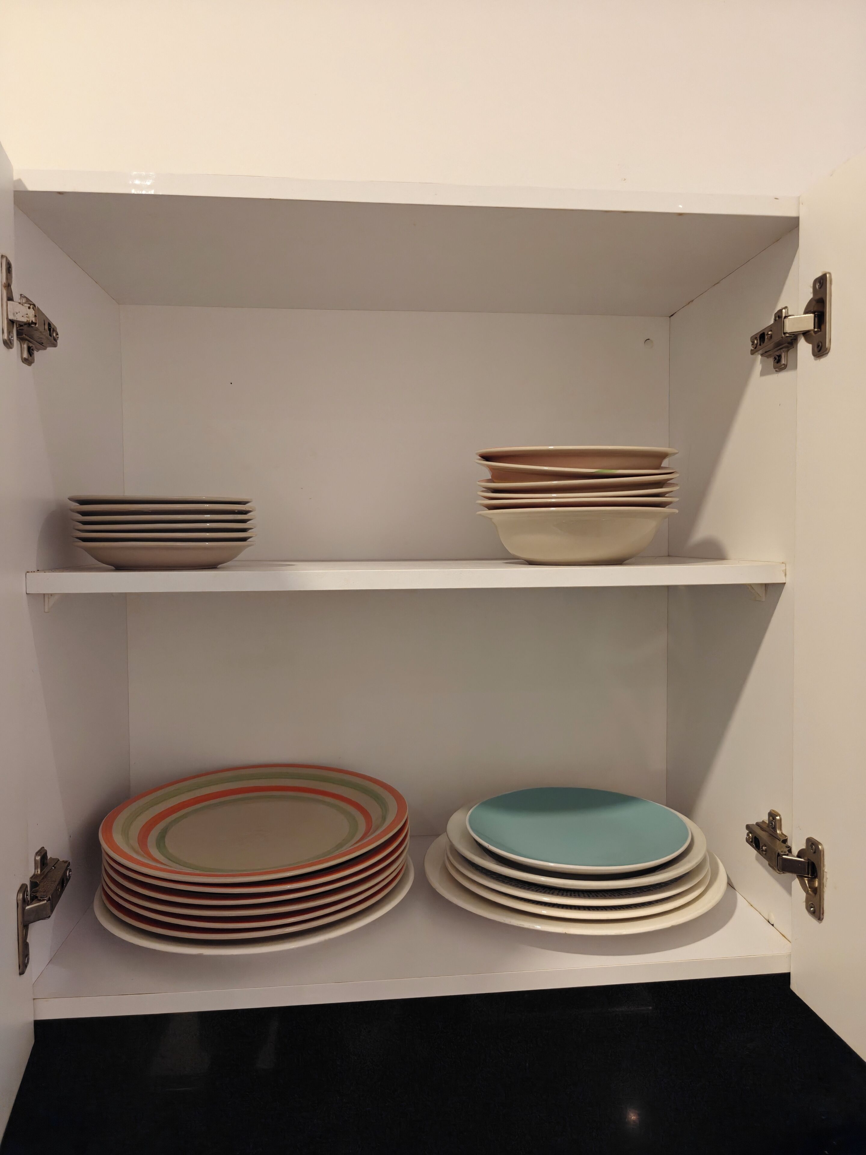 A kitchen cabinet with two shelves, each holding stacks of plates.