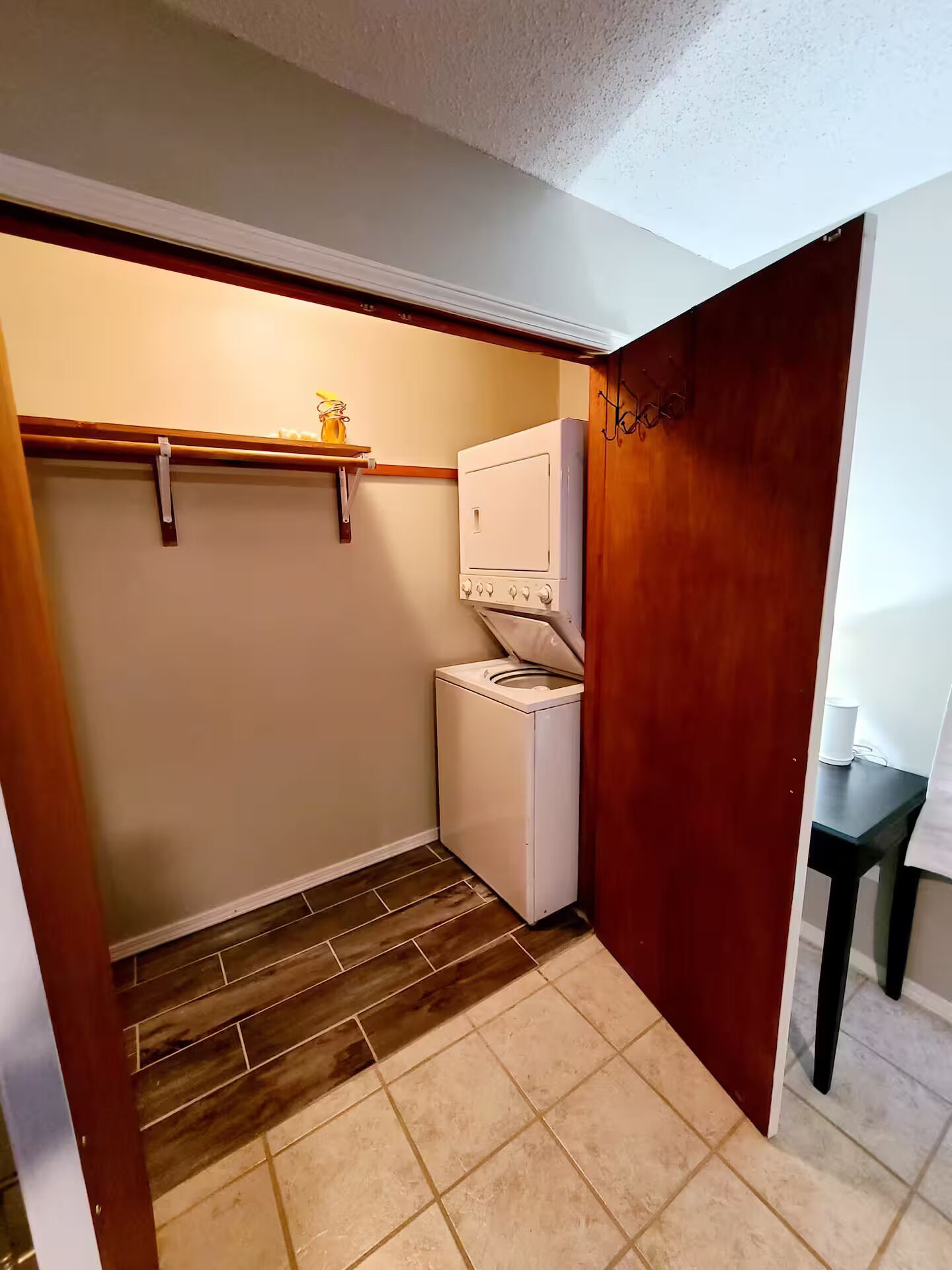 Un lavadero con lavadora y secadora, suelo de madera y una estantería con un tarro.